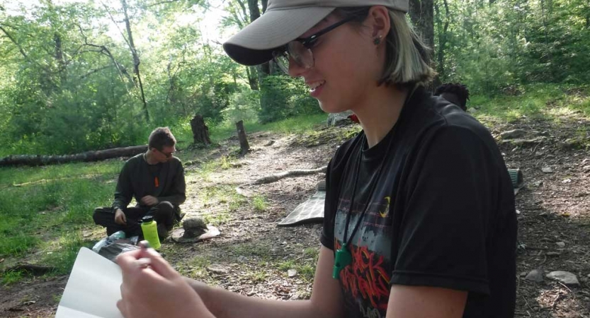 A person sits in a wooded area journaling 